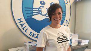 Anna von Zweygbergk på Håll Skärgården Rens kontor i Åbo. anna står framför en stor skylt av håll skärgården ren