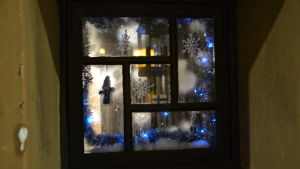 Julbelysning i grannhuset As oy Kellonsoittaja. Ett källarfönster med glitter, tomtar och Finlands flagga.