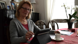 Inger Wretdal tycker att Almahemmet ska hållas i kommunal regi. Inger Wretdal med papper på bordet som har en röd bordduk. Fotat lite i motljus, Wretdal knäpper på sin dator och har en massa papper på bordet.