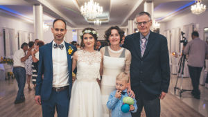 Bröllopsfest i Poznańområdet i västra Polen, hösten 2019. Från vänster: brudparet Tom och Kasia samt bröllopsgäster Aleksandra, hennes son Jan och Tadeusz som skrev denna text. En man med kort hårt i mörk kavaj och vit skjorta och fluga står tätt bredvid en kvinna i vit spetsbroderad bröllopsklänning med vita blommor i håret och tätt intill henne står en kvinna i mörkt hår med vit klänning med mörka axelband och