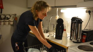 I kontorsstädningen ingår att ta hand om personalens disk och lägga igång diskmaskinen i personalrummet. Kvinna plockar i diskmaskin.