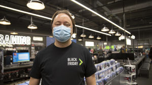 I Finland använder de flesta butiksanställda numera munskydd eller visir. Den här bilden togs i en butik i Vanda i slutet av november. En anställd vid elektronikaffären Gigantti som står inne i butiken med munskydd på sig. Personen har en t-skjorta på sig där det står "black friday".