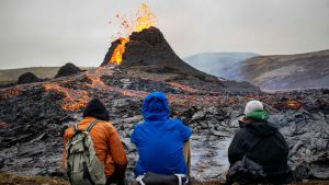 Många vill beskåda vulkanutbrottet. 22.3.2021. Tre personer som sitter och tittar på vulkanutbrottet på Island