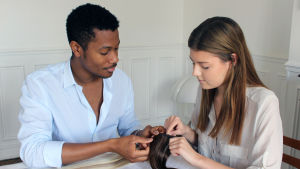 Emelie har lärt sig en massa bra knep under tiden med Harold. En man och en kvinna sitter vid ett bord. I händerna håller de löshår. De är make up-artister och hårstylister.