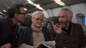 Nej, vi vill fortfarande inte att du skriver en biografi över Joe! Nathaniel (Christian Slater, Joan (Glenn Close) och Joe (Jonathan Pryce). Joan (Glenn Close) sitter i ett flygplan och ser irriterad ut, omringad av Nathaniel (Christian Slater) och Joe (Jonathan Pryce) som pratar med varandra.
