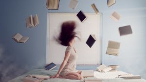 Nuori nainen istuu sängyllä, kirjoja lentelee hänen ympärillään.