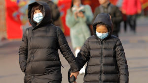 Ansiktsmasker är obligatoriska i Wuhan i flera stora provinser med över 300 miljoner invånare. Två personer håller i händerna. De har munskydd på sig och är klädda i svarta vinterjackor. Bilden är från Peking och tagen 21.1.2020.
