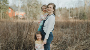 Rebecka väntar sitt tredje barn - hen förväntas komma i maj. Rebecka står höggravid på en äng med sin yngsta dotter i famnen och håller sin andra dotter i handen. Hon ler någonstans utanför bild.