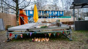 Under det här flaket hittades offret tre dagar efter mordet. Kynttilöitä ja kukkia Koskelan murhapaikalla. Taustalla rakennustyömaan parakit.