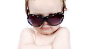 Vi måste ändå vara överens om att den här babyn är cool. En baby med solglasögon tittar mot kameran med armarna i kors.