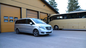 Forsbloms nya taxibil. En stor silverfärgad bil står bredvid en gul buss utanför ett garage.