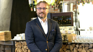Kim Juntunen, verksamhetsledare vid Lauluakatemia, tycker den klassiska musiken passar bra på slottet. En man med mustasch, mörka glasögon och kavaj ler mot kameran. En bar i bakgrunden.