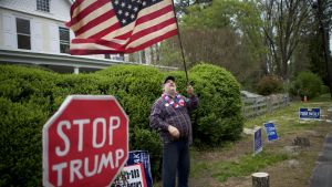 Demokraternas mål är att få bort Trump. Biden anses vara en kandidat som kan klara det. Demonstrant med amerikansk flagga och "Stop Trump"-trafikskylt