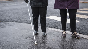 Blinda och föreningar för blinda eller synskadade har också fört fram krav på ljud från tysta bilar. Benen av två personer som står intill ett övergångsställe. Den ena person har i handen en vit käpp som används för personer med synnedsättning.
