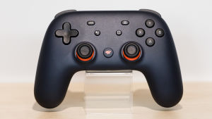 Google Stadia har en egen kontroll som är sladdlös om man spelar via Chromecast. Spelar man via en telefon eller PC krävs en USB-sladd. En svart spelkontroll med knappar i orange.