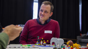 Mikael Öhman använder själv lego i sin undervisning. En man i röd tröja vid ett bord med legobitar.