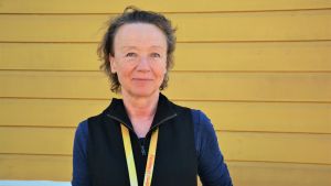 Laura Hollsten som är docent i historia leder projektet från Åbo Akademis sida. Laura Hollsten, en brunhårig kvinna som är klädd i en blå tröja och en svart väst står framför en gul vägg