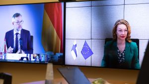 Europaminister Tytti Tuppurainen diskuterar med Tysklands europaminister Michael Roth över videolänk. Ett fotografi av två videoskärmar. På den ena ser vi en bild av Finlands Europaminister Tytti Tuppurainen och på den andra en bild av Tysklands minister Michael Roth.