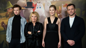 Edvin Endre, Jennifer Saunders, Rosamund Pike ja Taron Egerton seisovat muumien kuvausseinän edessä vierekkäin hymyillen.