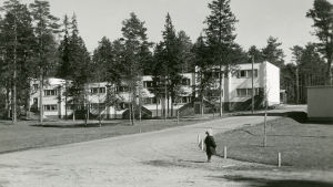 Mäkelä var arbetsledningens hus. Liten pojke står på en sandväg, i bakgrunden ett nybyggt vitt tvåvåningsradhus. Bilden är svartvit och tagen på 1950-talet.