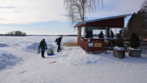 Matti och Risto drar i väg på fiskefärd. Två personer med pulka i färd med pimpelfiske.