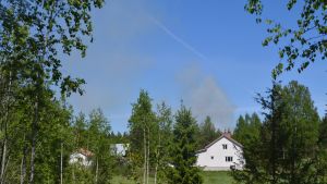 Röken från skogsbranden syns ovanför trädtopparna i Forsby. Rök från skogsbrand bakom hus i Lovisa