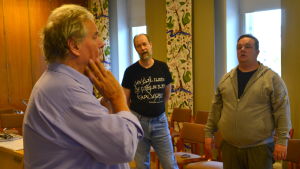 Leif Lindblom (i mitten) får tips på hur man mjukar upp kinderna. Teppo Salakka leder Runebergskören under övning.