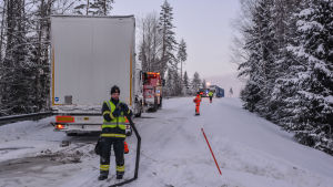 Brandman samlar upp slang medan bärgningsbilen drar iväg olyckslångtradaren