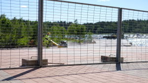 På bostadsområdet i Sibbostrand har man börjat snygga upp området. En man packar sand med en maskin bakom ett metallstaket.