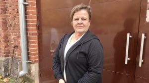 Ansa Holm är glad att så många kommit till Osteoporosförbundets evenemang i Åbo. Ansa Holm står vid en metalldörr utomhus.