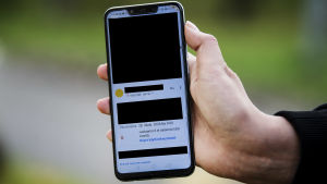 Efter att tiotusentals personer blivit offer för utpressning i samband med dataintrånget på Vastaamo, har redan kring 25 000 personer gjort en brottsanmälan. En hand som håller i en telefonskärm där man ser ett okrypterat meddelande som Vastaamo skickat. Stora delar av meddelandet har svarta rutor på sig för att gömma mottagarens personuppgifter.