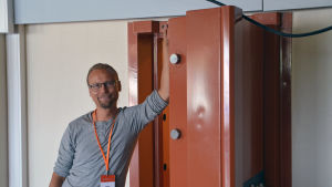 Tommi Paju framför dörren till sitt rum. Dörren är så massiv för att påminna om att det tidigare har funnits en bank i huset. Bild på Tommi Paju som är ungdomsledare i Pyttis.
