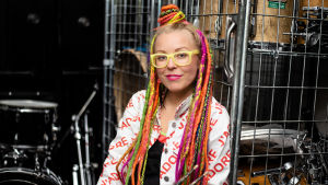 Trummor i alla färger och former fascinerar Vicky. Vicky Österberg med färglada dreadlocks framför trummor.