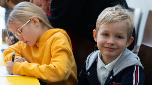Noel Hellöre. I bakgrunden pysslar systern Erin julkort. BUU-dagen i Hfors 2019. Porträtt.