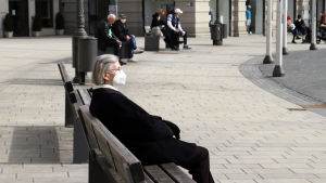 Invånare i Augsburg en söndagseftermiddag. En dam med munskydd sitter på en bänk i staden Augsburg