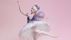 Prinsessa Ruusunen. Ballerina taikasauva kädessään vaaleanpunertavaa taustaa vasten.
