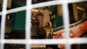 En robot lyfter ut toalettsolen efter att den gjutits. Arbetsplatsen är inhägnad så att ingen kommer i närheten och blir skadad. En orange robotarm lyfter en wc-stol på Ido badrum i Ekenäs.