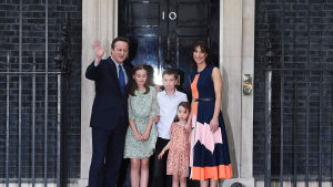 David Cameron tillsammans med sina tre barn och frun Samantha utanför premiärministerns bostad 10 Downing Street innan han åkte till Buckingham Palace. David Cameron tillsammans med sina tre barn och frun Samantha utanför premiärministerns bostad 10 Downing Street med en svart dörr med siffran 10 på.