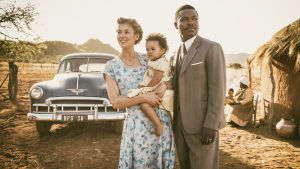 Rosamund Pike spelade den ena huvudrollen i filmen A United Kingdom. Här ses hon tillsammans med den andra huvudrollsinnehavaren, David Oyelowo. Ruth (Rosamund Pike) håller i dottern och bredvid henne står maken Seretse (David Oyelowo).
