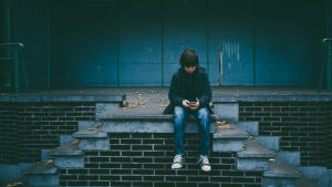 Håll koll på vad ditt barn använder sin telefon till. Pojke sitter med telefon på trappa.