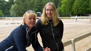 Tävlingsledare Mia Maukonen och deltagaren Carolina Grahn från Hangö. Mia Maukonen och Carolina Grahn lutar mot ett staket vid gamla sportplan i Hangö.