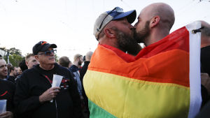 Ett par invirade i en regnbågsflagga kysser varandra i San Francisco vid Harvey Milk Plaza dit människor samlats för att sörja, hedra och minnas offren i masskjutningen i Orlando.