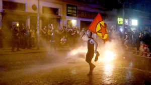 En demonstrant viftar med en rödgul flagga, framför en eld som demonstranterna startat på gatan i Hamburg.