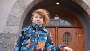Joshua Heselius sitter med i skolans elevkår. Åttaåring i halvbild framför skolbyggnad.