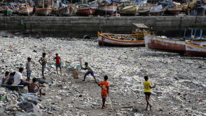 Barn i Indien spelar cricket på en strand fylld med plastskräp. Strand i Indien.