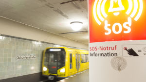 Tåget anländer till plattformen på Schönleinstrasse, i förgrunden en telefon för nödsamtal.