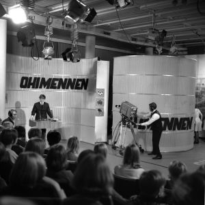 Tv-ohjelman tekeminen. "Ohimennen"-ohjelman kuvaukset tv-studiossa. Juontaja Markku Veijalainen puhuu yleisölle