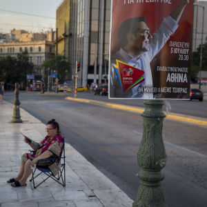 Många greker ställer sig likgiltiga till valet. Valaffisch med vänsterpartiet Syrizas ledare Alexis Tsipras. I bakgrunden sitter en äldre dam till synes likgiltig på en stol.