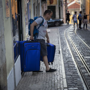Många turister väljer ett kortvarigt hyreskontrakt istället för hotell. Turist bär på två tunga väskor på en gata i Lissabons historiska centrum.