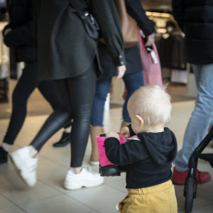 De vuxnas munskyddsbeklädda ansikten intresserar inte Kerttu lika mycket som andra barn utan munskydd. Kerttu Ranta-Panula går omkring bland människor i ett köpcentrum.